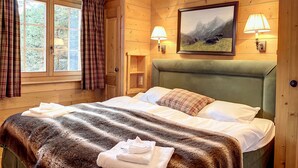 A wooden-paneled room with a bed, two bedside lamps, a painting of mountains, and a window with curtains. - Bastide 014, Optimal sun exposure, quiet, central location (Verbier)