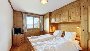 Une chambre dans une cabane en bois, avec un lit, une télévision et une fenêtre avec des rideaux.