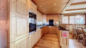 Une cuisine en bois dotée d’appareils électroménagers intégrés, un coin repas avec des chaises en bois et une fenêtre laissant entrer la lumière naturelle.