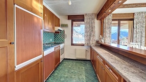 A compact kitchen with wooden cabinets, a green patterned backsplash, and a view of the mountains through a window. - Living room with fireplace, kitchen bar with vitroceram, Nespresso coffeemachine and dishwasher, thr (Verbier)