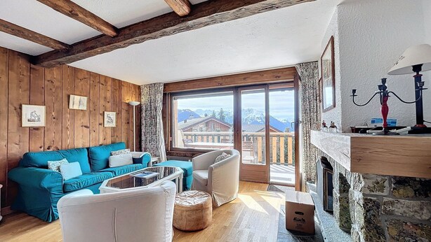 A cozy living room with wooden walls, a blue sofa, a white armchair, and a fireplace. - Living room with fireplace, kitchen bar with vitroceram, Nespresso coffeemachine and dishwasher, thr (Verbier)