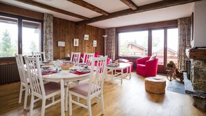 A dining area with a wooden table and chairs, a red sofa, and a stone fireplace. - Living room with fireplace, kitchen bar with vitroceram, Nespresso coffeemachine and dishwasher, thr (Verbier)