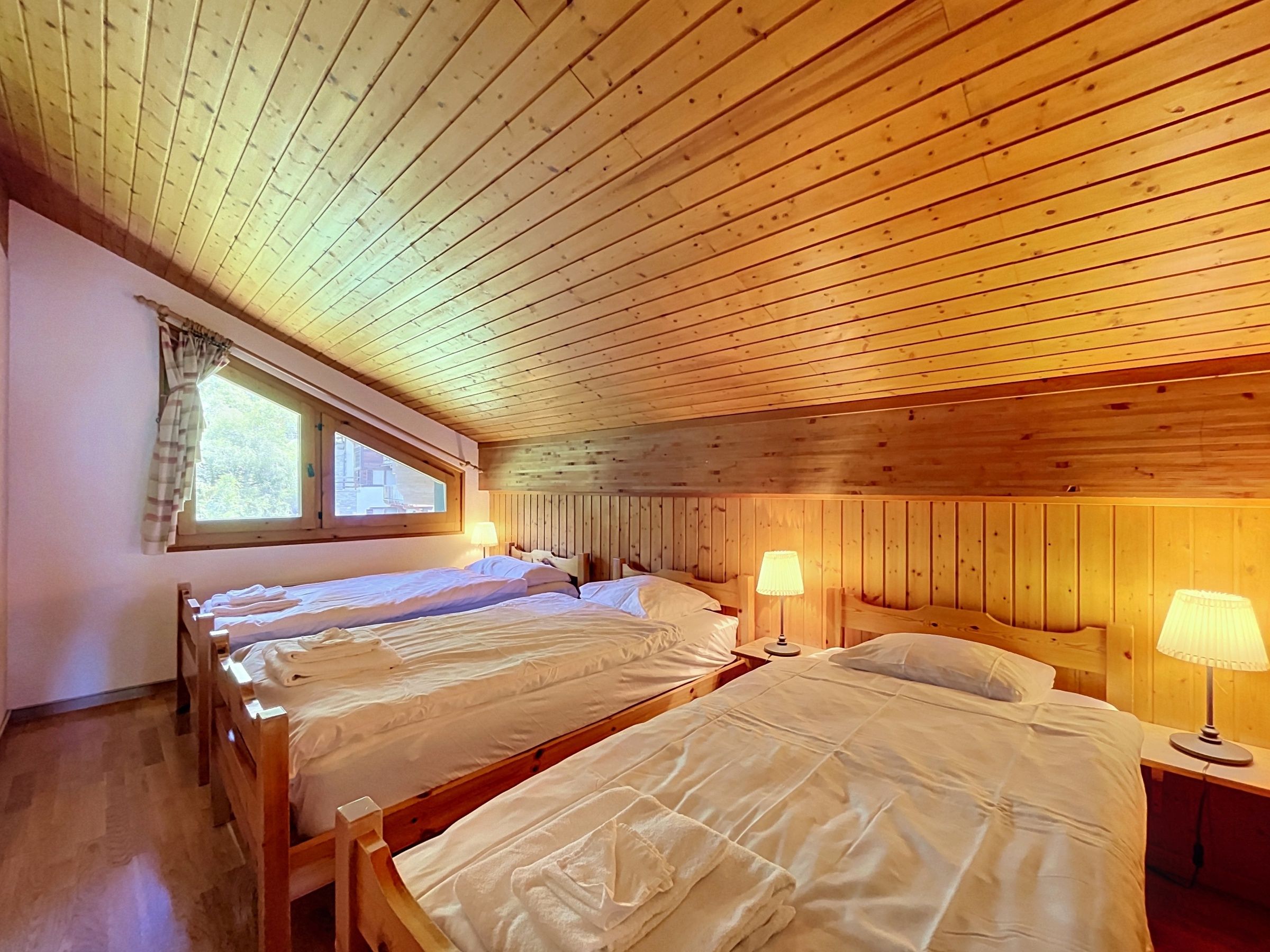 Habitació amb parets i sostre de fusta, dos llits amb llençols blancs, una finestra amb cortines i dues làmpades de nit.