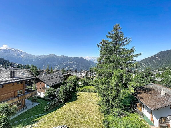 A residential area with houses, a large coniferous tree, and a mountain range in the background. - Diure 222, quiet, central location (Verbier)