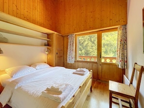 A wooden room with a bed, a chair, and a window with curtains.