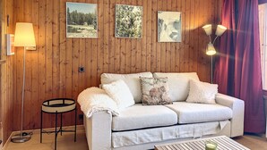 Ett mysigt rum med en väggpanel av trä, en vit soffa med dekorativa kuddar, en golvlampa och inramade tavlor.