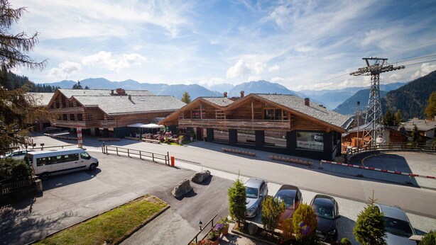 En fjällstuga med trähus, en parkeringsplats och utsikt över avlägsna berg.