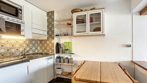 Una cocina compacta con armarios blancos, una mesa de madera y un microondas.