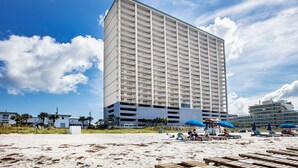 Een hoog hotel met meerdere verdiepingen en balkons, gelegen aan een strand met heldere lucht.
