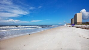 Een strand met een zandstrand, golven en een stadsachtergrond.