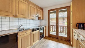 A kitchen with wooden cabinets, a tiled backsplash, a dishwasher, and a stove. - Living room with fireplace and eating corner,, kitchen with 3 hotplates and dishwasher, one bedroom (Verbier)