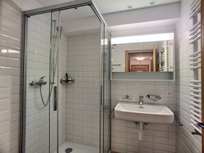 Une salle de bain moderne avec une douche à parois de verre, un lavabo avec un miroir au-dessus et un porte-serviettes.