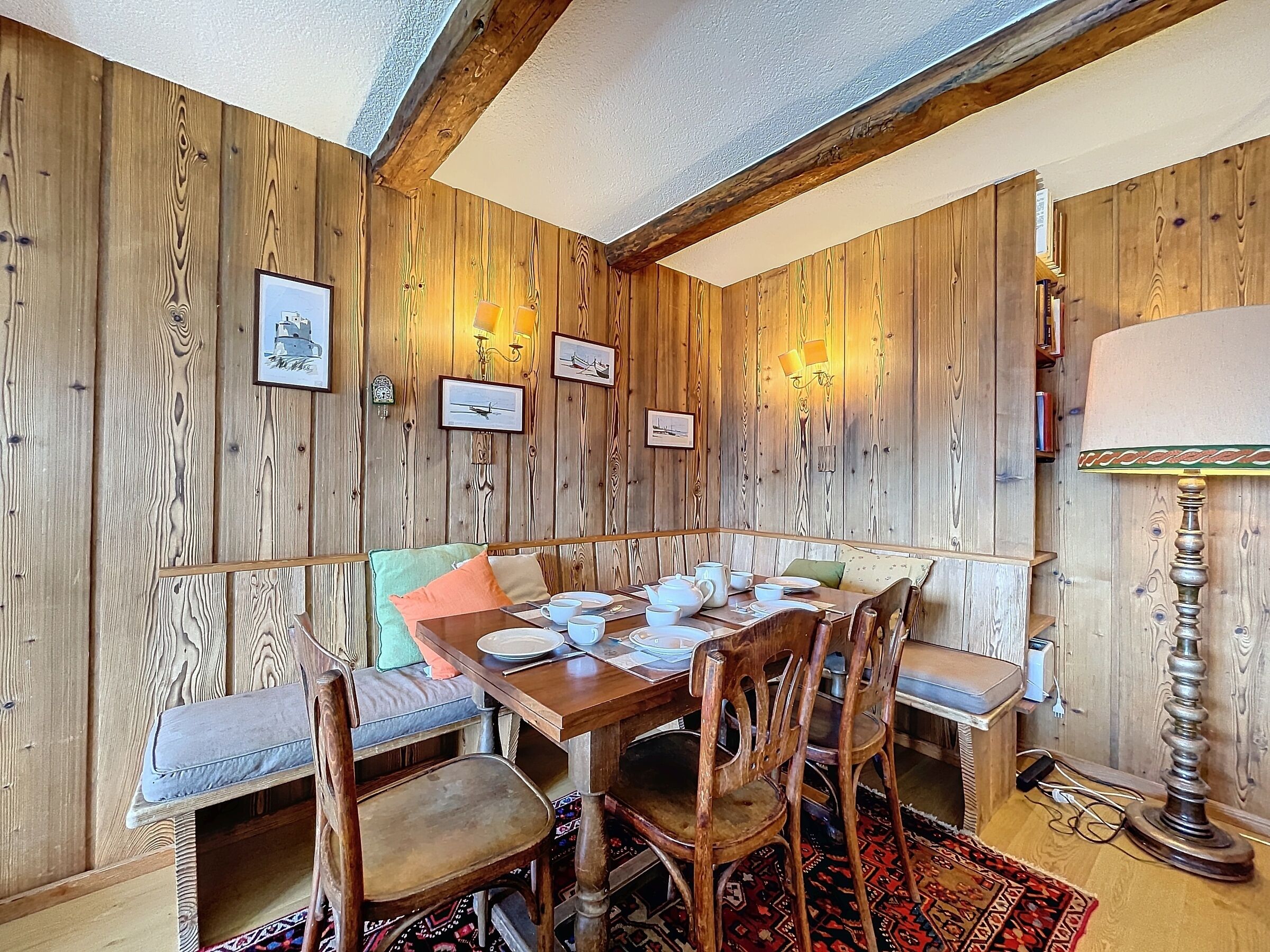 Une pièce aux murs lambrés, avec une table à manger dressée pour quatre personnes, entourée de chaises et de bancs en bois.