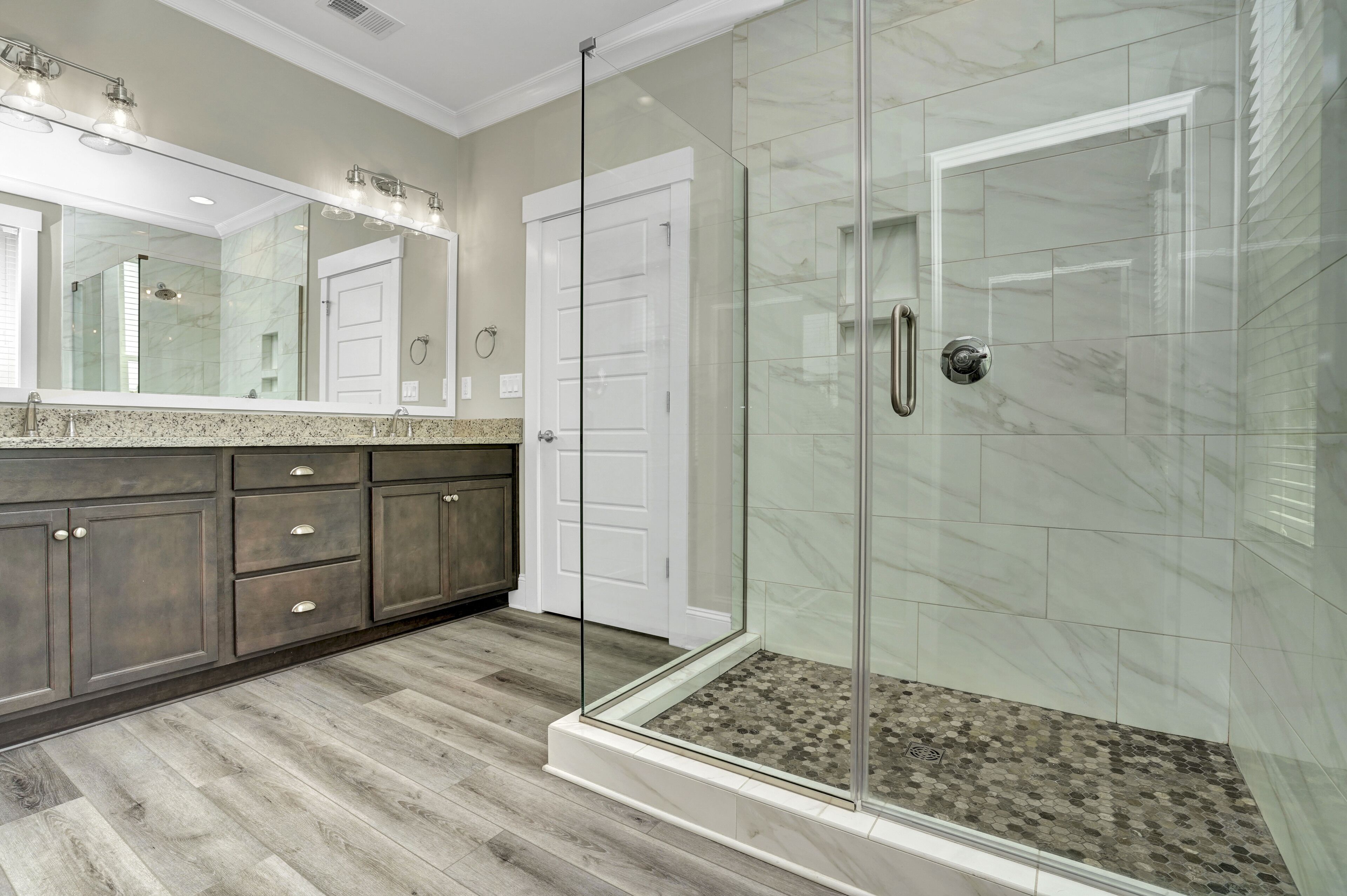 A modern bathroom with a glass-enclosed shower, a large mirror, and dark wood cabinetry.