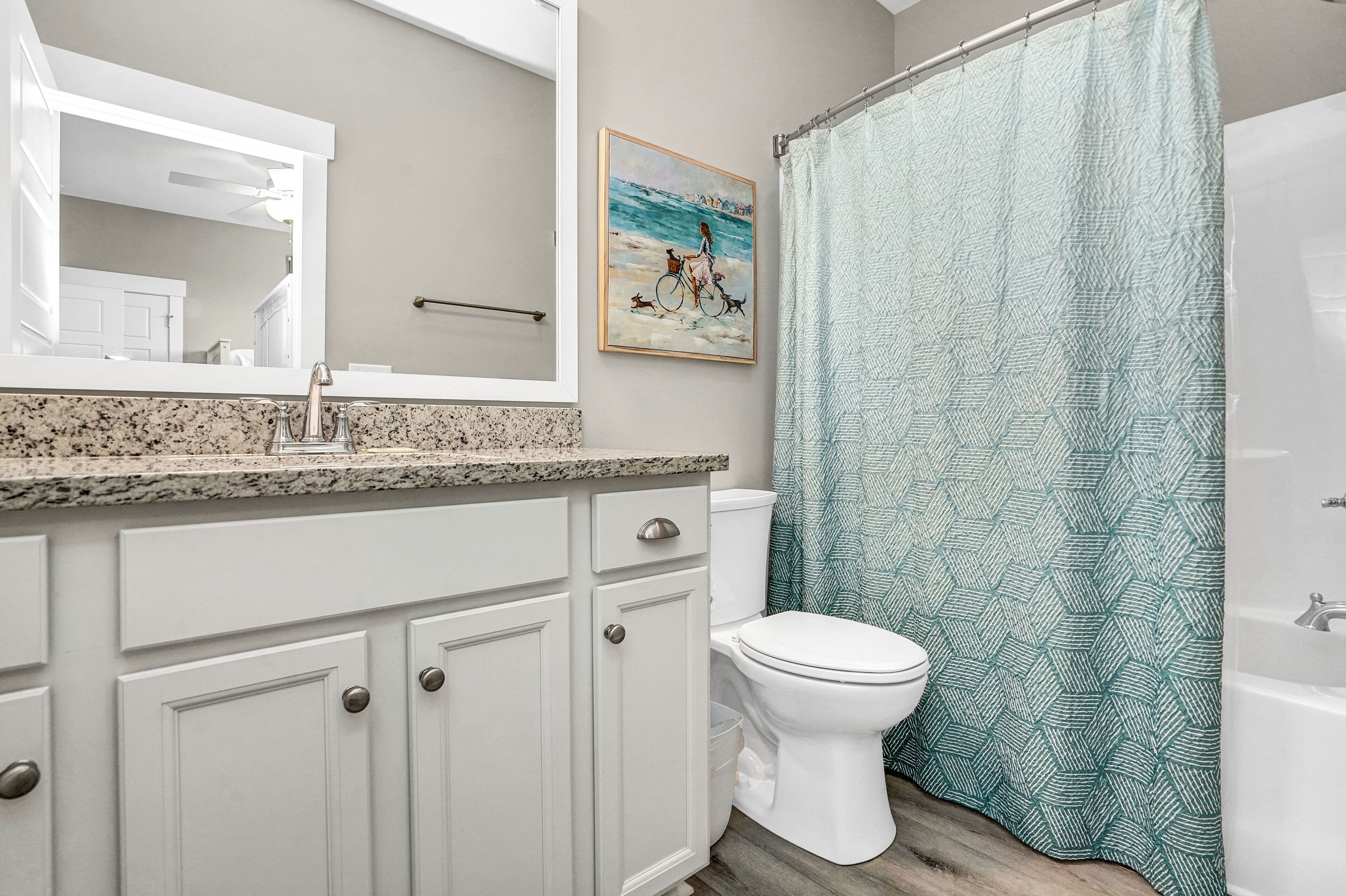 Une salle de bain avec des toilettes blanches, un lavabo doté d’un plan de travail en granit et un rideau de douche à motifs géométriques.
