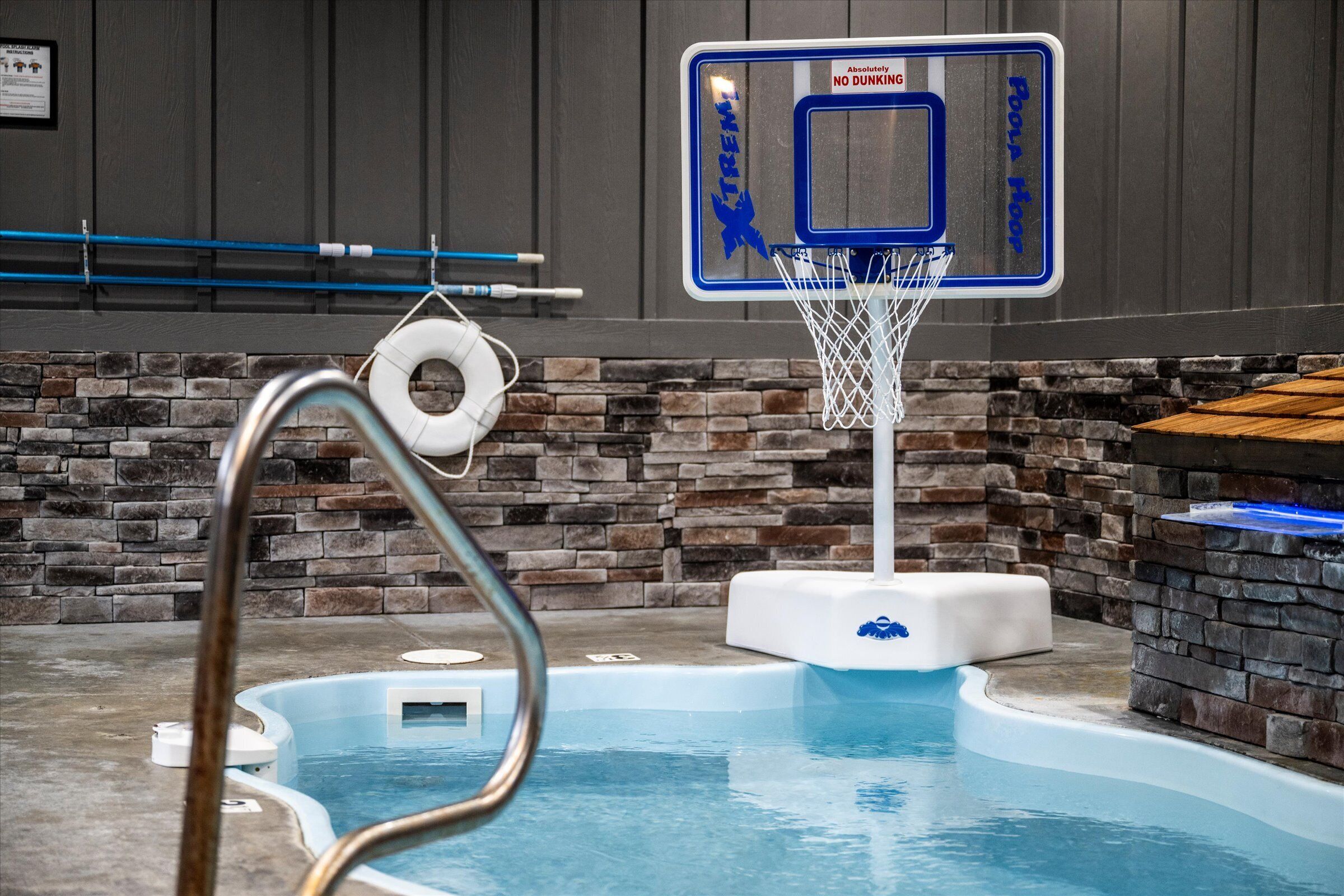 Piscina interna con canestro da basket, parete in pietra e vasca idromassaggio.