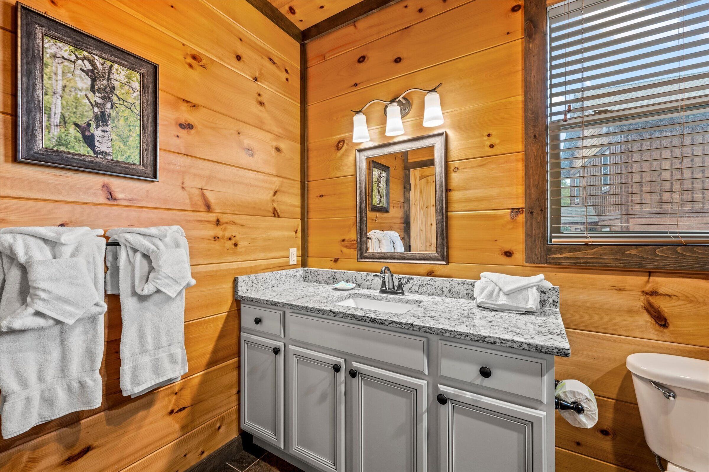Baño de cabaña de madera con lavamanos de encimera de granito, un espejo y toallas colgadas en la pared.