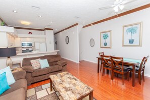 A living room with a brown sofa, a coffee table, and a dining area with wooden chairs and a glass table.
