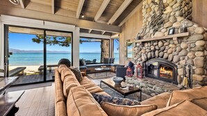 A spacious living room with a stone fireplace, a large sofa, and a view of the ocean. - Newly renovated Lake Tahoe Beachfront #635 (South Lake Tahoe)