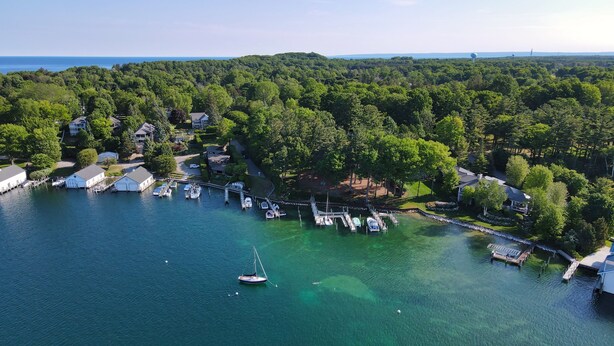 An aerial view of a marina with boats docked, surrounded by dense forest and residential properties.