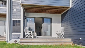 A modern building with a covered porch, two white folding chairs, and a glass door leading to an interior space.