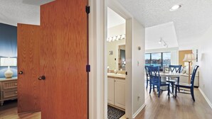 A modern kitchen with white cabinets, a dining area with blue chairs, and a view through a glass door.
