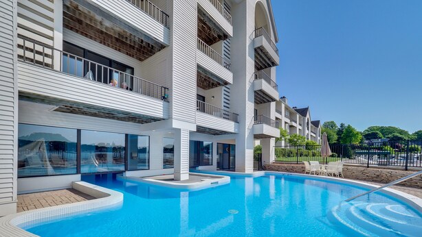 A modern hotel with a large indoor swimming pool, multiple balconies, and a clear view of the surrounding area. - Edgewater Inn 117 C | Waterfront Access| Pool, Hot Tub, Sauna | Sleeps 4 (Charlevoix)
