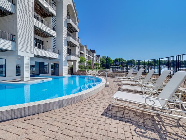 A swimming pool with lounge chairs and a building with balconies. - Edgewater Inn 117D | Waterfront Access | Pool, Hot Tub, Sauna (Charlevoix)