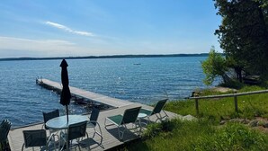 Ein Seeufer mit einer Terrasse, einem Tisch, Stühlen, einem kleinen Boot und weiter Blick auf das Wasser und die Uferlinie.