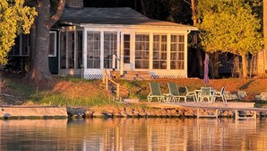 Een vakantiehuis aan het meer met een overdekt terras, buitenmeubels en uitzicht op het water.