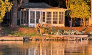 A lakeside cabin with a covered porch, outdoor seating, and a view of the water.