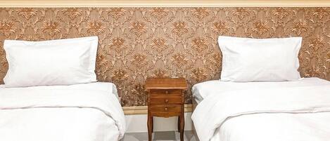 Ein Hotelzimmer mit zwei Betten, einem Holfnachtkästchen und einem Kopfende mit Blumenmuster.