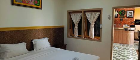A hotel room with a bed, a headboard, a window with curtains, a wall-mounted air conditioner, and a framed picture.
