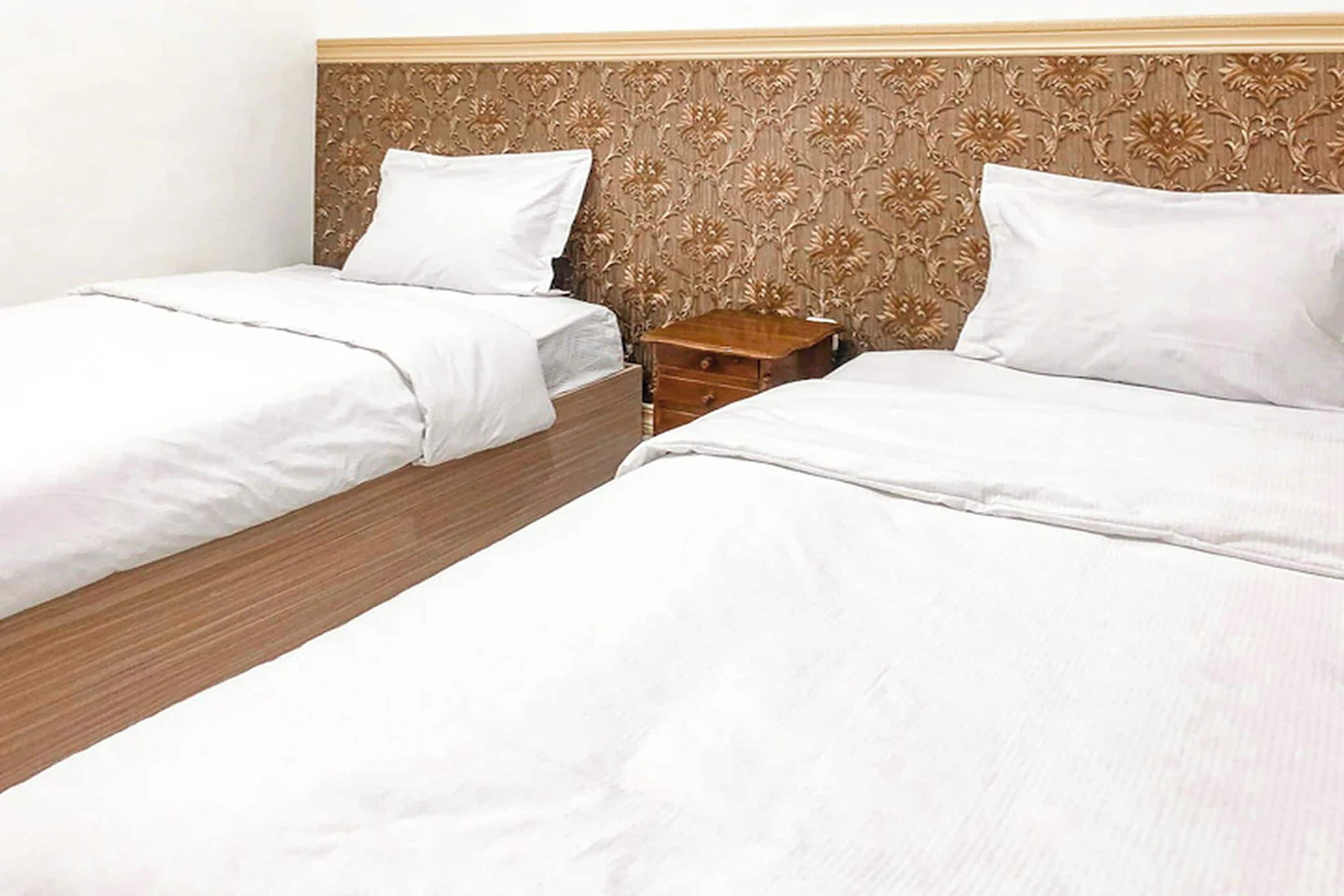 Two single beds with wooden headboards and white bedding, a wooden nightstand, and a patterned wall.
