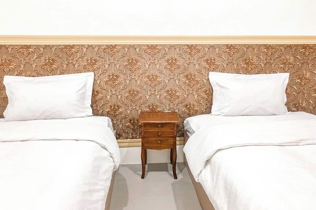 A hotel room with two beds, a wooden nightstand, and a floral-patterned headboard.