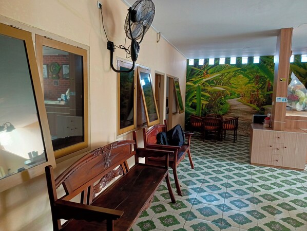 A room with wooden benches, a fan, a wall clock, and a mural of a tropical landscape. - Adisa Homestay by Zuzu (Malang)