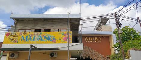 A building with a sign reading 'ADISA HOMESTAY' and a colorful banner above.