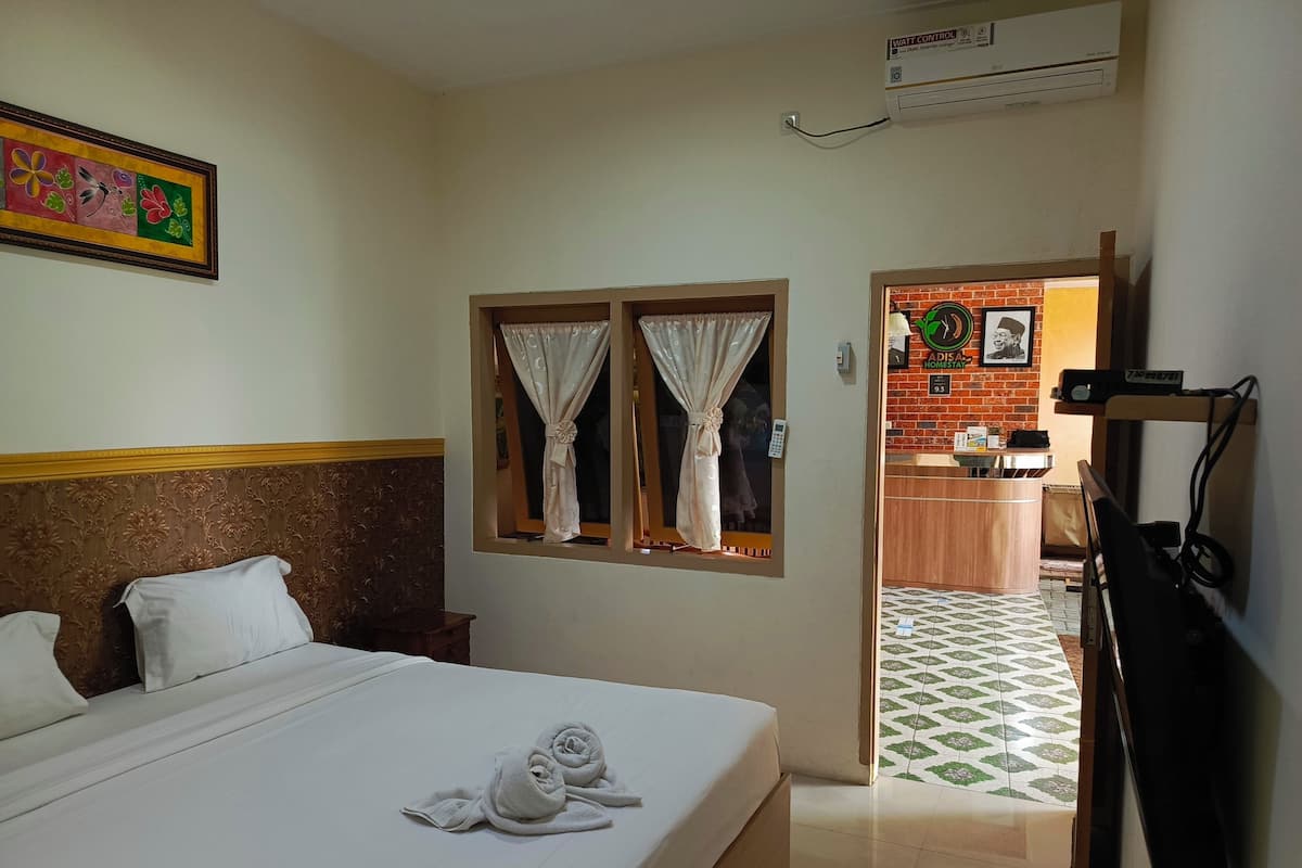 A hotel room with a bed, a window with curtains, a wall-mounted air conditioner, and a framed picture.