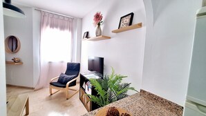 Un salon comprenant un téléviseur, un fauteuil, une plante et une étagère ornée d’objets décoratifs.