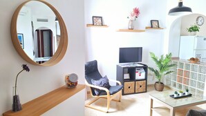 Un salon moderne avec un grand miroir, un fauteuil confortable, un téléviseur et une table basse en verre.