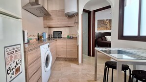 Une cuisine moderne équipée d’un lave-linge intégré, un coin repas avec une table en verre et un salon avec un canapé.