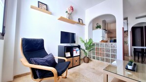 Un salon avec un fauteuil bleu foncé, un téléviseur à écran plat et un petit meuble contenant des objets décoratifs.