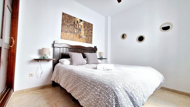 Une chambre à coucher comprenant un lit, deux tables de chevet, une œuvre d’art accrochée au mur et trois découpes circulaires dans le mur.