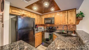 A kitchen with granite countertops, wooden cabinets, a black refrigerator, a microwave, and an oven. - SS B4 Riverside Condo (New Braunfels)