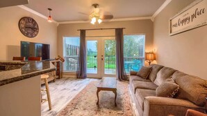 A living room with a sofa, a coffee table, a TV, and a clock on the wall. - SS B4 Riverside Condo (New Braunfels)