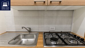 A kitchen with a stainless steel sink, a gas stove, and wooden cabinets.