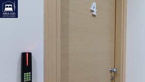 A wall-mounted electronic keypad with a red light, a wooden door with the number 4, and a door handle.