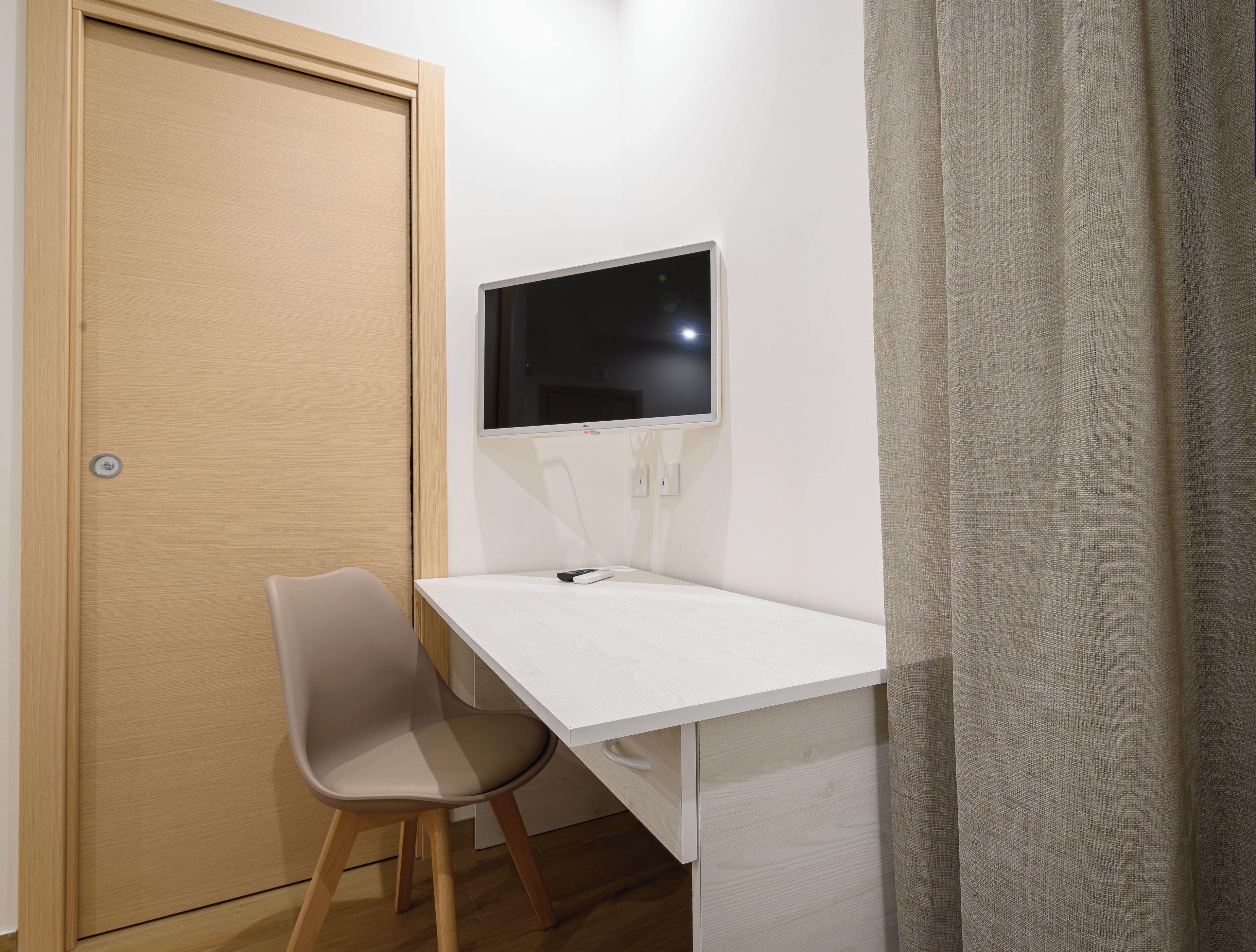 Une petite pièce privée, avec un bureau blanc, une chaise, un téléviseur et une porte.