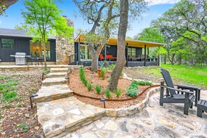 A modern outdoor patio with stone steps, a grill, and Adirondack chairs. - Red Bird Cottage- Convenient 2/1 with Outdoor Space (Wimberley)
