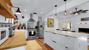A modern kitchen with white cabinetry, stainless steel appliances, wooden shelves, and pendant lighting. - Red Bird Cottage- Convenient 2/1 with Outdoor Space (Wimberley)